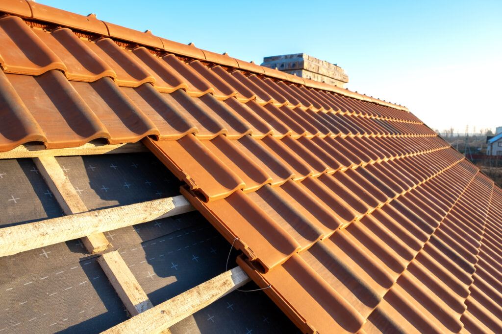 Overlapping rows of yellow ceramic roofing tiles mounted on wooden boards covering residential building roof under construction.