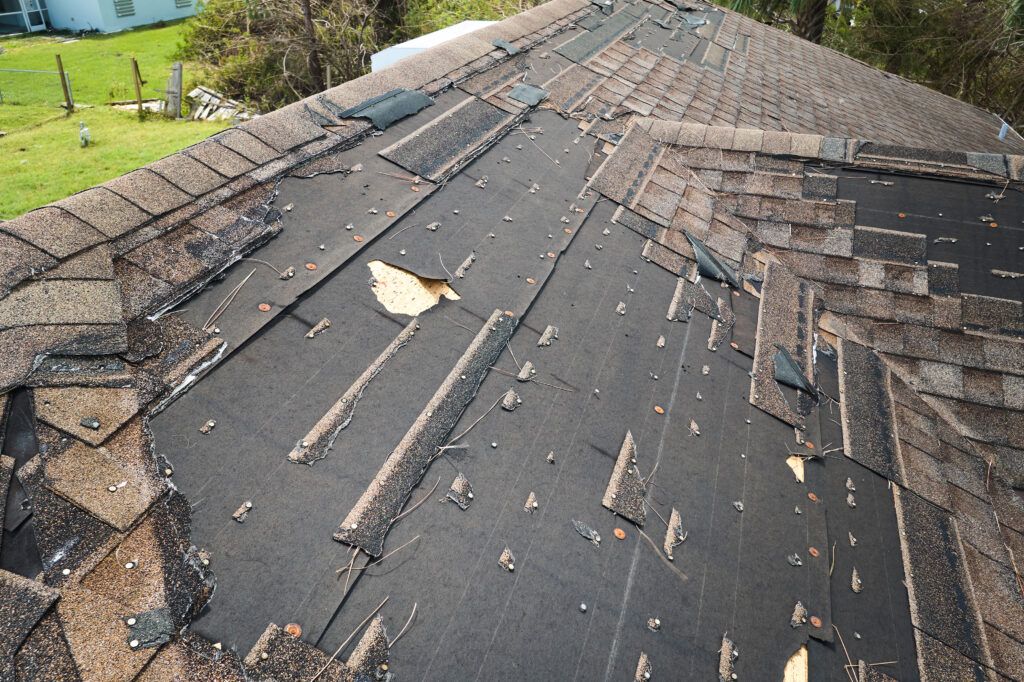 Wind damaged house roof with missing asphalt shingles after hurricane Ian in Florida. Repair of home rooftop concept.